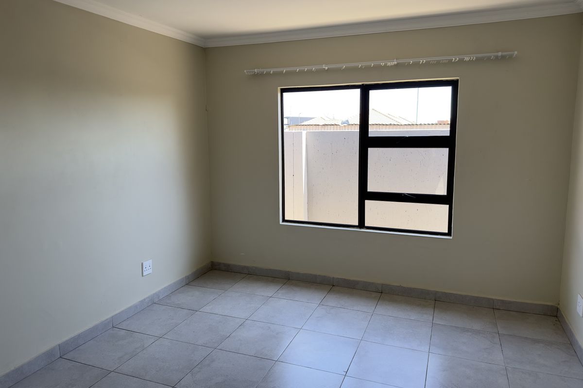 A vacant bedroom featuring neutral wall paint, tiled flooring, and a large window with a black frame.