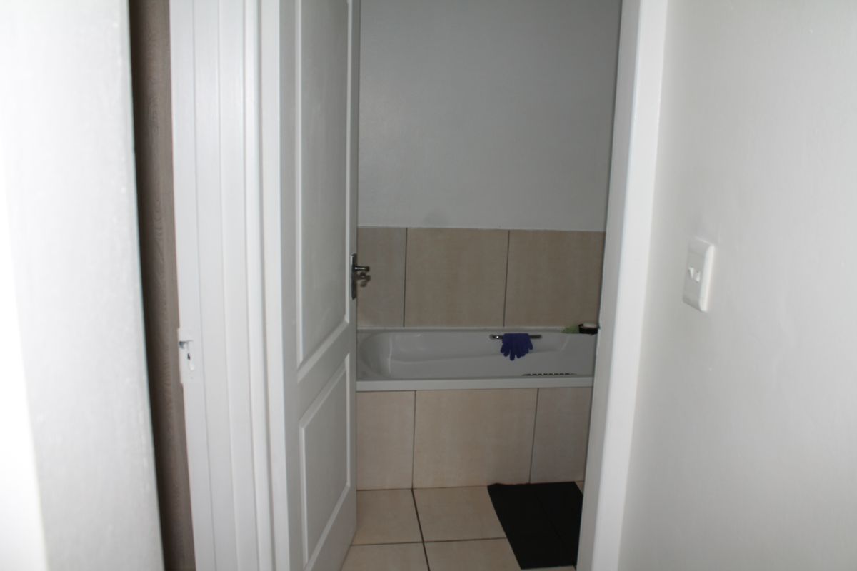 A view into a bathroom featuring a built-in bathtub with neutral wall and floor tiling.