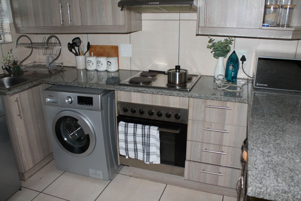 A functional kitchen featuring wood-look laminate cabinetry, granite countertops, a built-in oven with hob, and an integrated laundry appliance space.