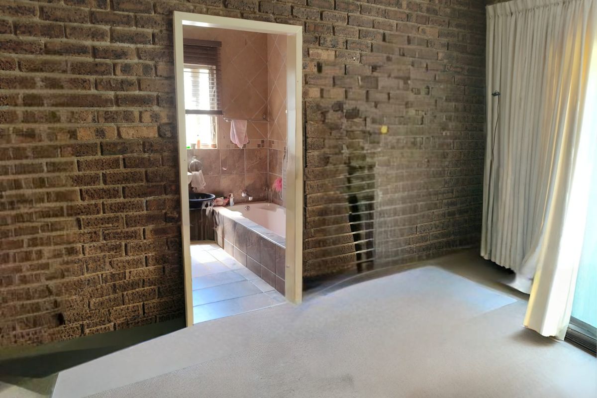 A bedroom featuring exposed brick walls and carpeted flooring, with an adjoining en-suite bathroom containing a built-in bathtub.