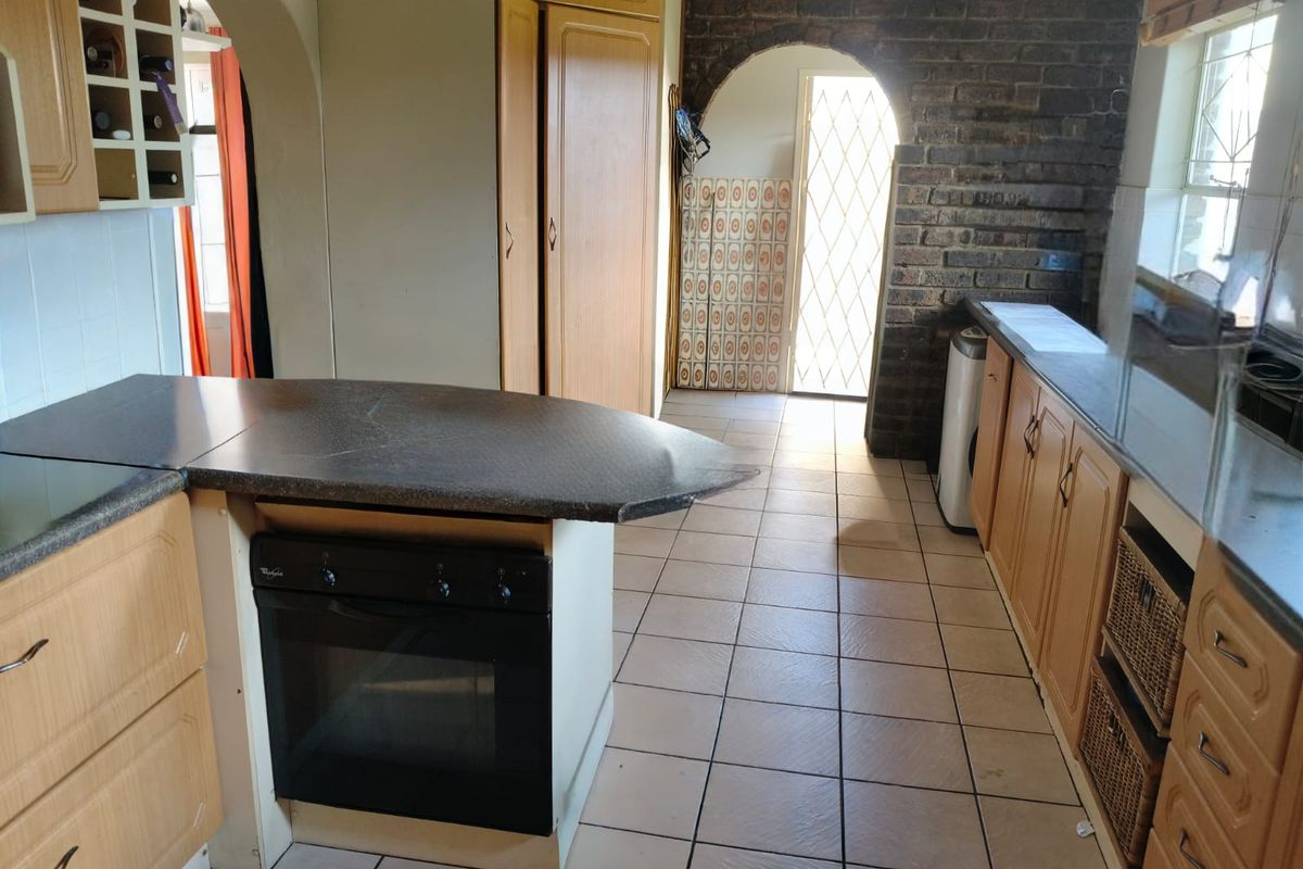 A functional kitchen featuring wooden cabinetry, a built-in oven, tiled flooring, and a distinctive brick archway leading to an exterior entrance.