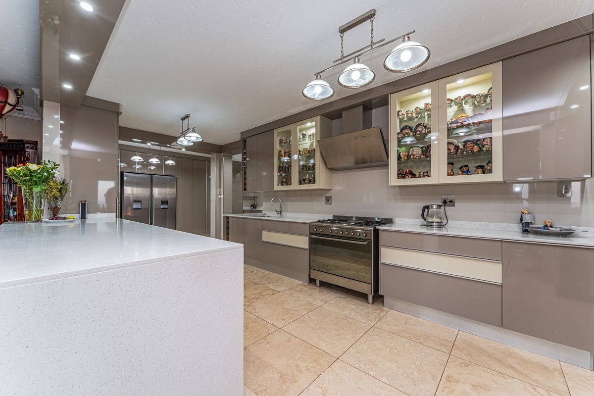 Modern kitchen featuring high-gloss cabinetry, stone countertops, a large central island, stainless steel gas range, and integrated lighting.