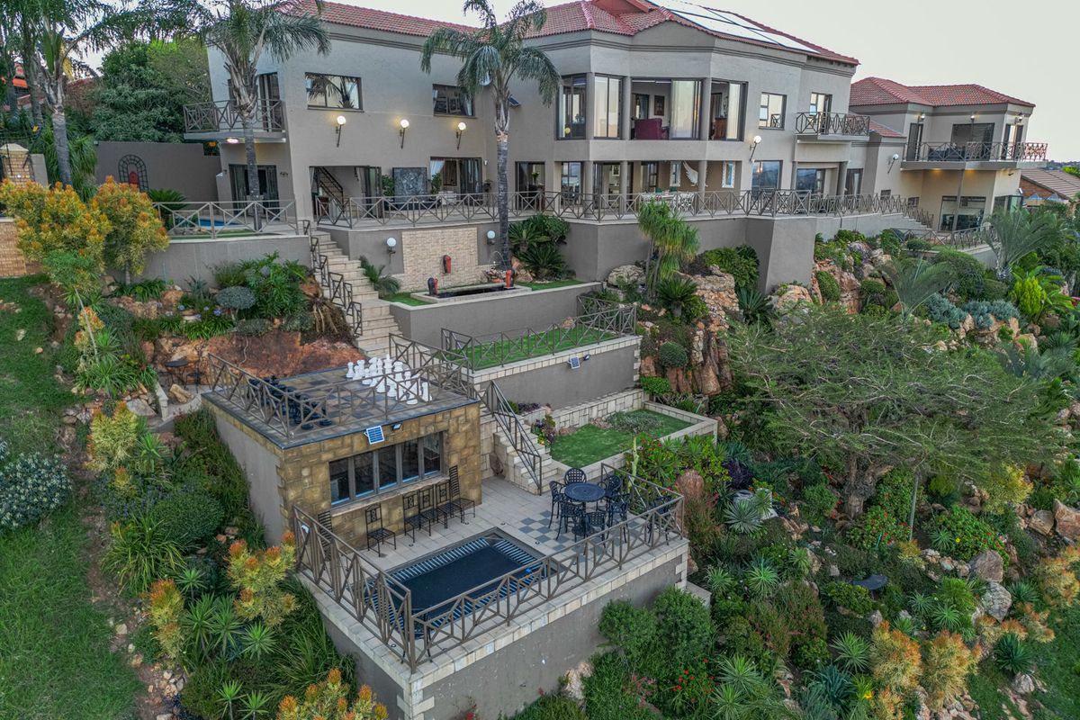 Aerial view of a multi-level residential property featuring extensive terraced landscaping, stone retaining walls, multiple balconies, and a lower-level entertainment area with a pool.