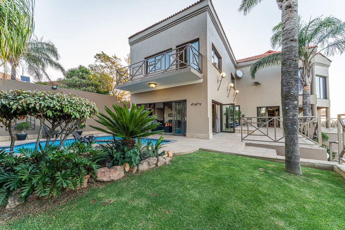 Rear view of the house featuring a swimming pool, landscaped garden, paved patio area, and a balcony accessible from the upper level.