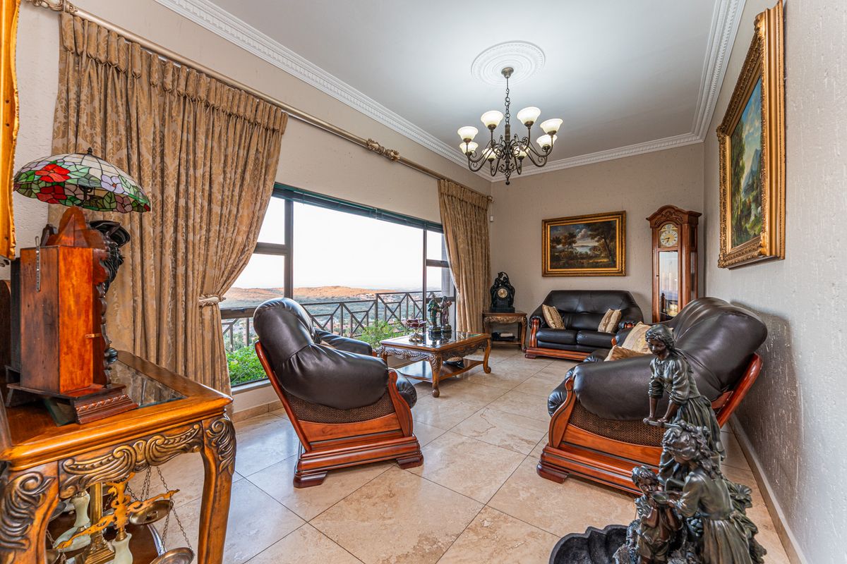 A formal living room featuring large windows with scenic views, tiled flooring, decorative ceiling rose, and a classic chandelier.