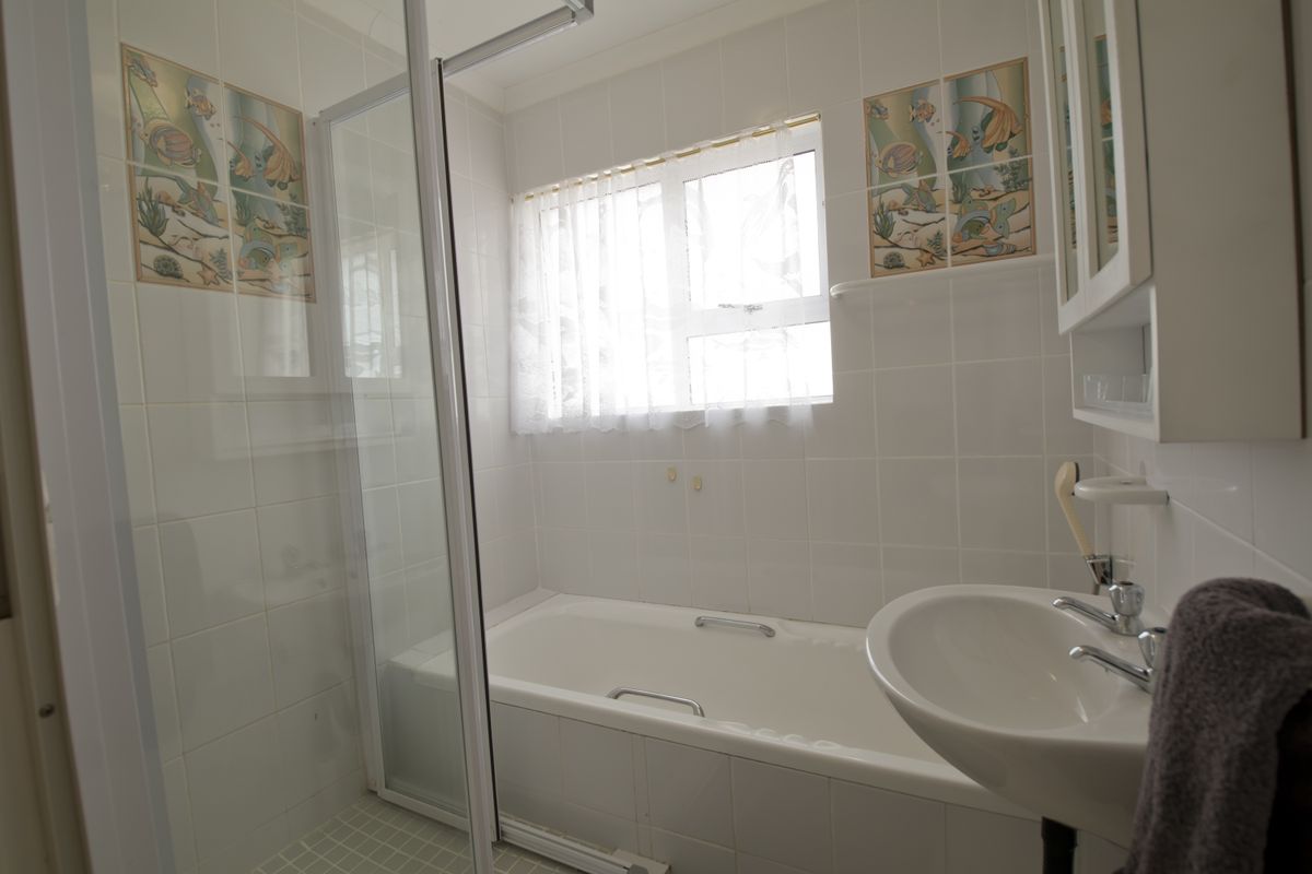 A functional bathroom featuring a white bathtub, a glass-enclosed shower, and a pedestal sink with wall-mounted cabinetry.