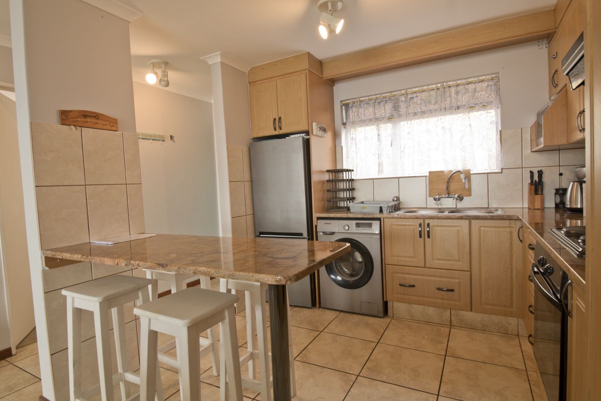 A functional kitchen featuring light wood cabinetry, granite-look countertops, tiled flooring, a built-in oven, and an integrated laundry appliance.