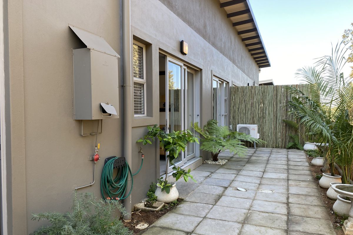 Rear exterior view of the apartment featuring a paved patio area, sliding door access, gas geyser installation, and privacy screening.