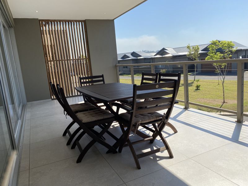 A spacious covered balcony featuring modern tiled flooring, a timber privacy screen, and metal railings, offering a pleasant outdoor living area.