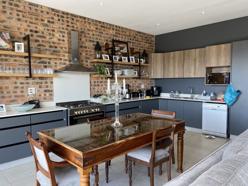 Modern open-plan kitchen featuring exposed brick walls, dark grey cabinetry, wood-look upper cabinets, and integrated appliances, seamlessly flowing into the dining area.