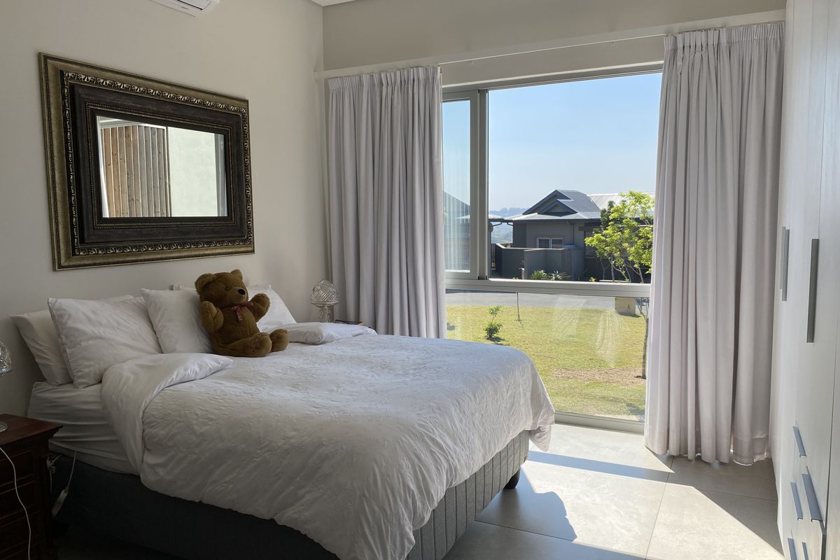A bright, modern bedroom featuring large windows with garden views, built-in cupboards, and an integrated air conditioning unit.