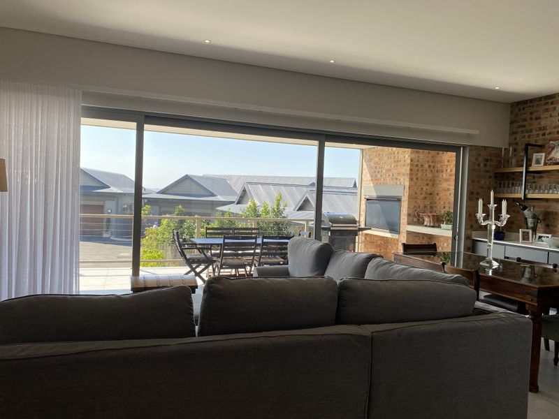 Spacious open-plan living area featuring large sliding doors, exposed brick accents, and a built-in braai, seamlessly connecting to the outdoor patio.