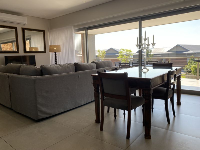 Spacious open-plan living and dining area featuring large sliding glass doors that open onto a balcony, complemented by modern tiled flooring and recessed lighting.