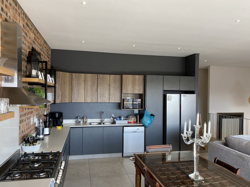 Modern open-plan kitchen featuring exposed brick walls, dark cabinetry, gas hob, and stainless steel extractor, seamlessly flowing into the living and dining area.
