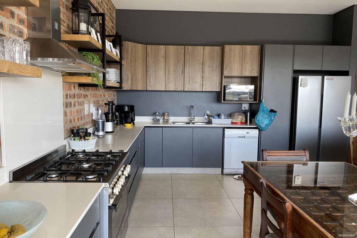 Modern kitchen featuring exposed brick walls, stone countertops, gas hob, extractor fan, and contemporary cabinetry with integrated appliances.