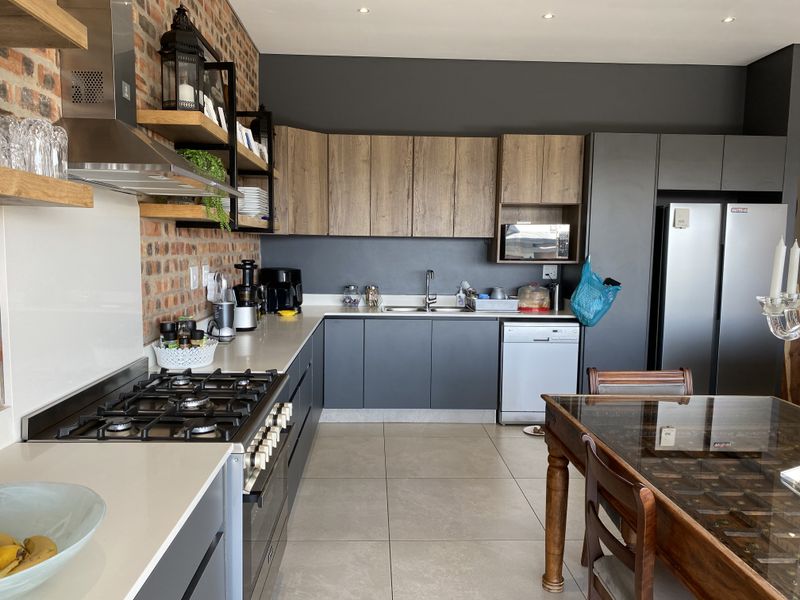 Modern kitchen featuring exposed brick walls, stone countertops, gas hob, extractor fan, and contemporary cabinetry with integrated appliances.