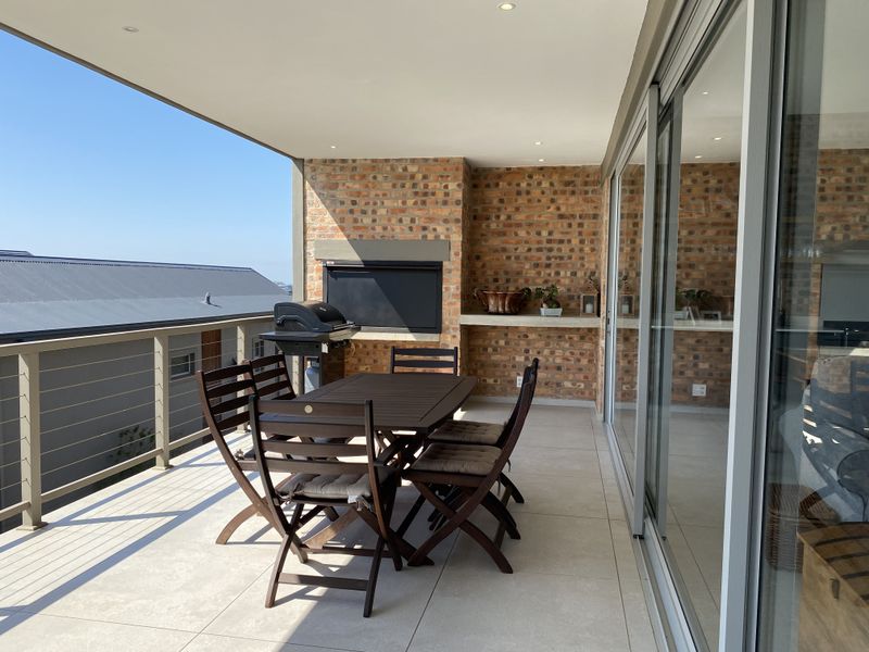 Spacious covered balcony featuring a built-in braai, brick feature wall, and large sliding glass doors providing seamless indoor-outdoor flow.