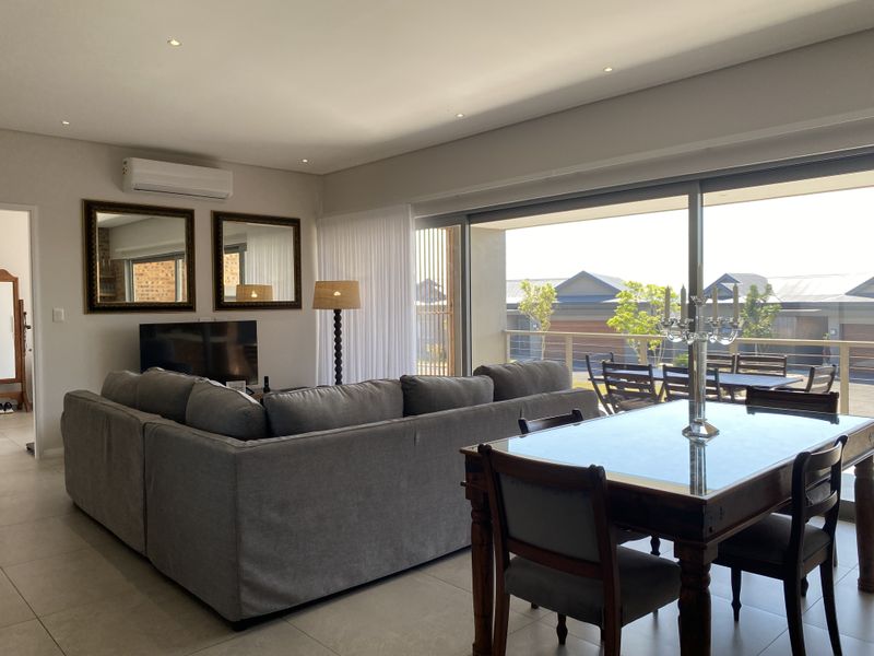 Spacious open-plan living and dining area featuring large sliding glass doors that open to a balcony, complemented by modern recessed lighting and tiled floors.
