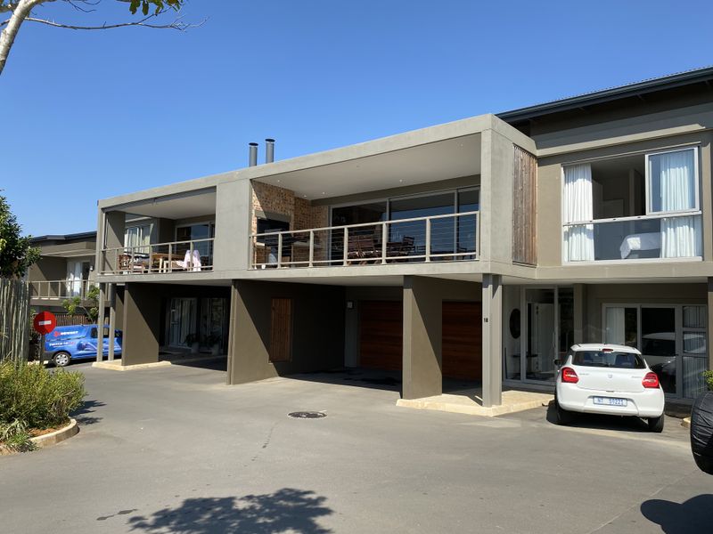 Modern apartment exterior featuring a spacious balcony with a built-in braai, ground-level garage access, and contemporary architectural finishes.