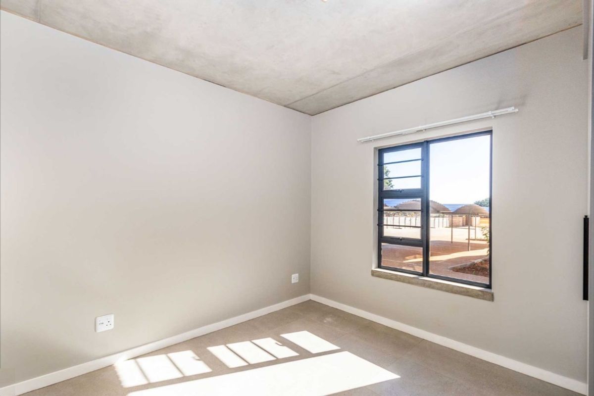 A bright, empty bedroom featuring neutral walls, a concrete-look ceiling, tiled flooring, and a window with a view of the exterior.