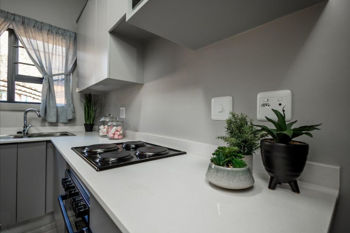 Modern kitchen featuring sleek grey cabinetry, white countertops, a built-in electric hob, and a stainless steel sink with a window view.