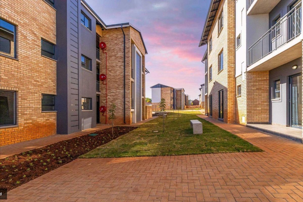 A view of the landscaped courtyard between apartment blocks, featuring brick paving, manicured lawn, and modern face-brick building facades.
