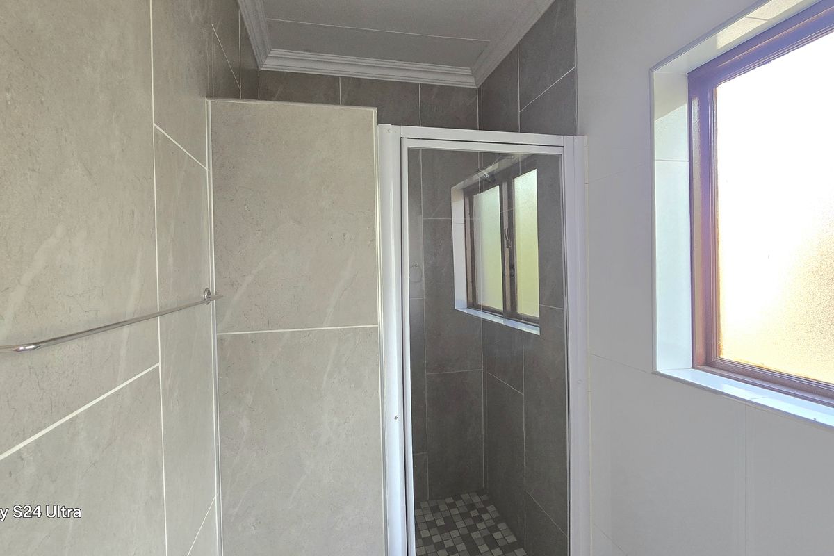 A clean, modern bathroom featuring a tiled shower enclosure, neutral wall tiling, and a window providing natural light.