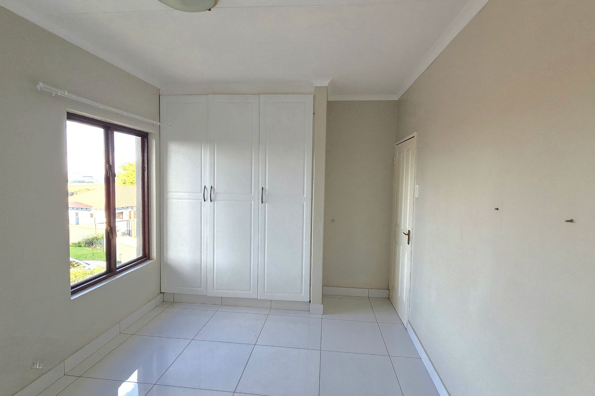 A bright, empty bedroom featuring neutral tiled flooring, built-in white cupboards, and a window providing natural light.
