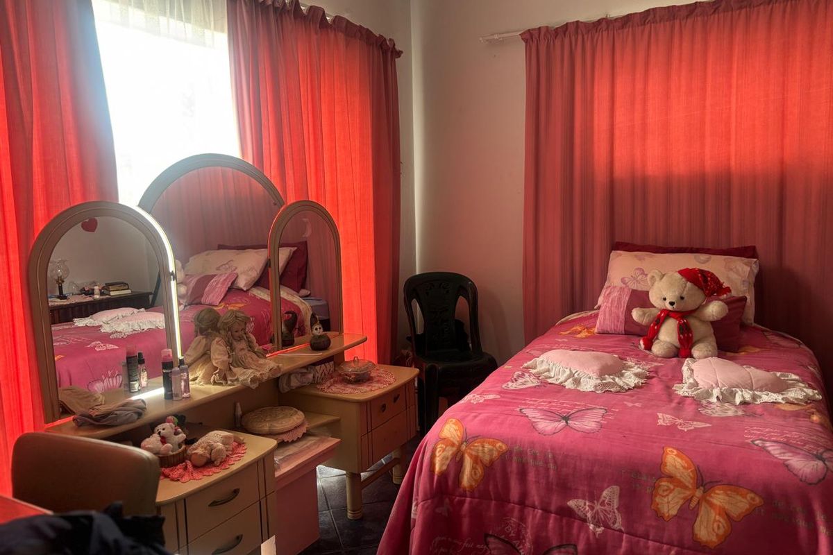 A bedroom featuring tiled flooring and large windows dressed with curtains, providing a functional space for rest.