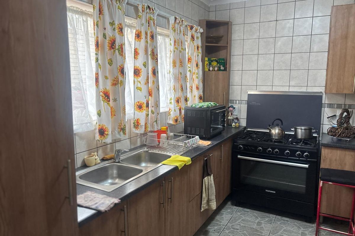 A functional kitchen featuring wood-look cabinetry, a double stainless steel sink, and a freestanding gas stove with an integrated extractor hood.