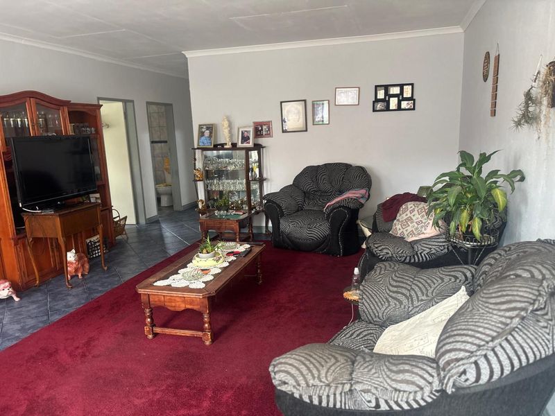 A spacious living room featuring dark tiled flooring, a large red carpet, and access to adjacent rooms.