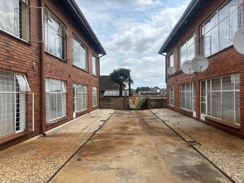 Exterior view of an apartment complex courtyard featuring brick facades, large windows with security bars, and a central concrete driveway area.