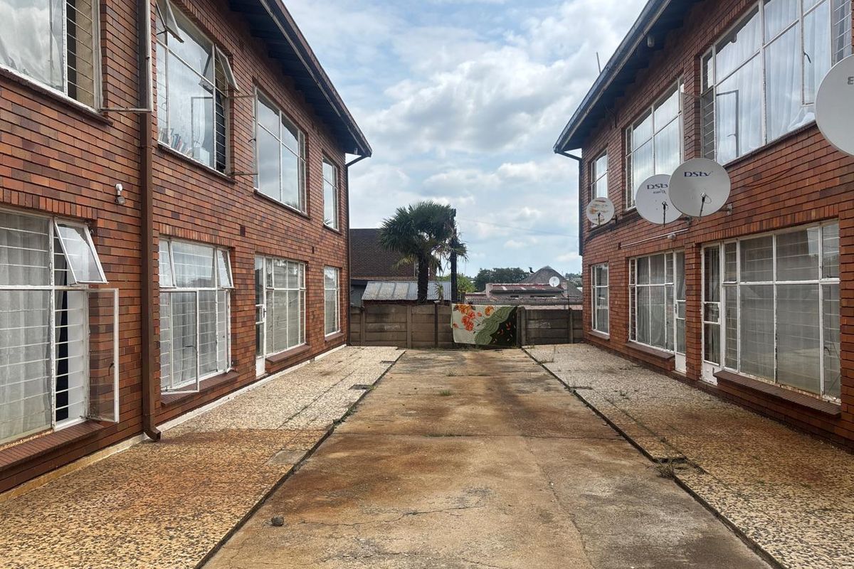 Exterior view of an apartment complex courtyard featuring brick facades, large windows with security bars, and a central concrete driveway area.