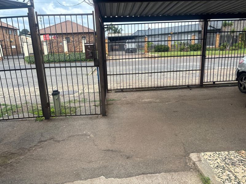 A covered carport area with metal security gates and asphalt flooring, providing secure off-street parking within the apartment complex.