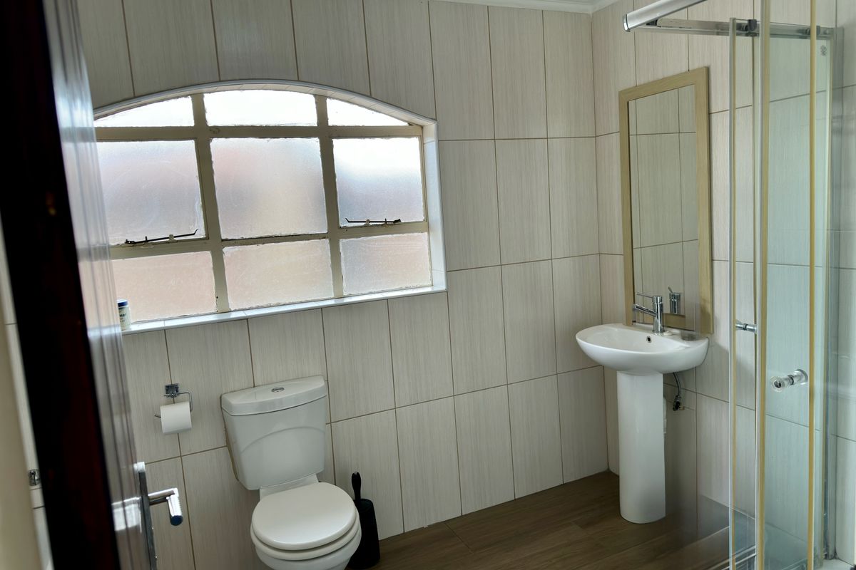 A functional bathroom featuring a pedestal sink, a toilet, and a glass-enclosed shower, finished with neutral wall tiling and wood-look flooring.
