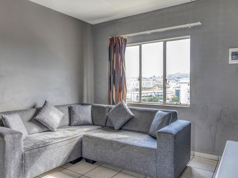 A living room featuring tiled flooring, an aluminium window with exterior views, and a wall-mounted electrical distribution board.