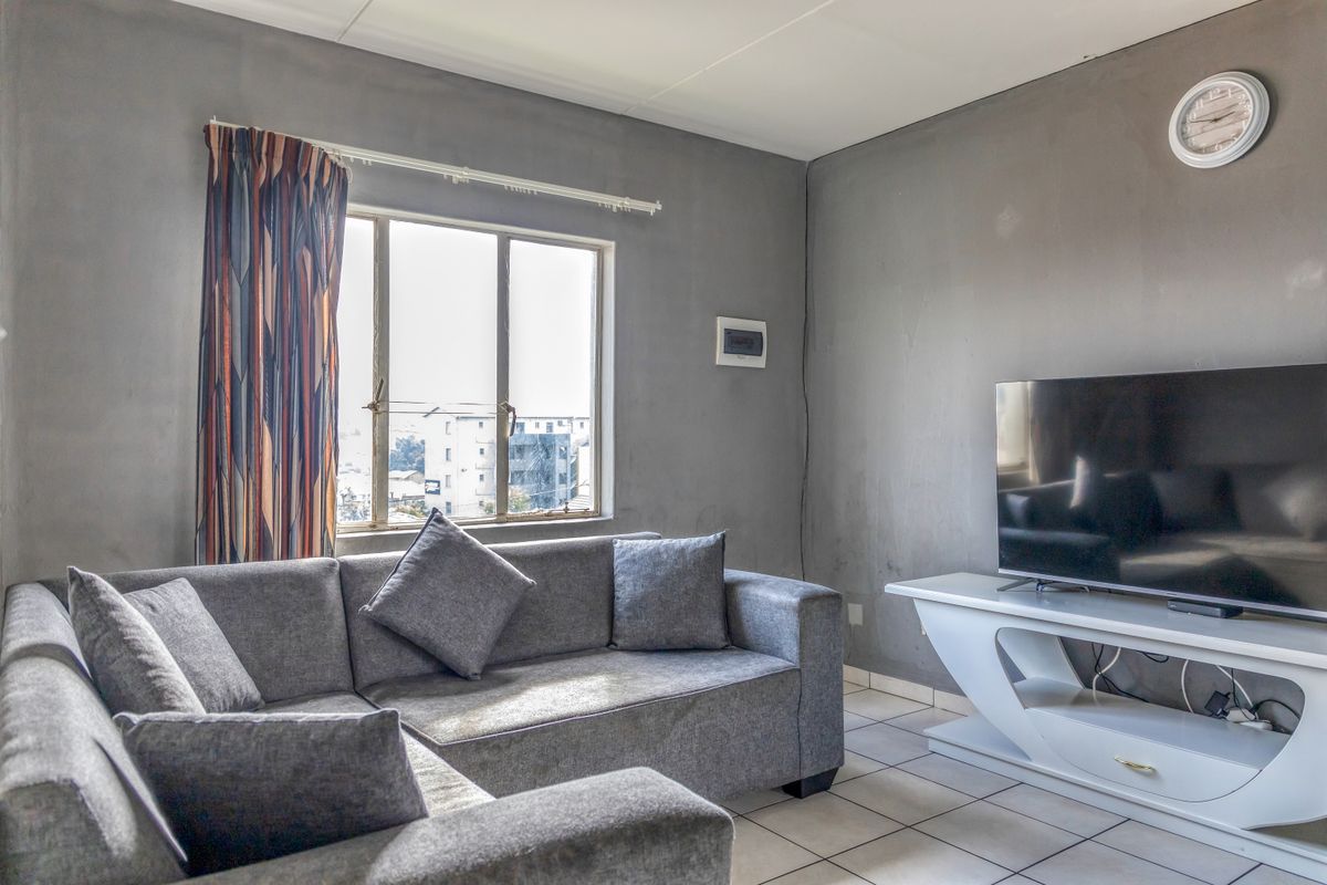 A living room featuring tiled flooring and an aluminium window. The walls show visible wear and scuffing, suggesting a need for cosmetic updates.