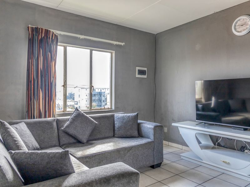 A living room featuring tiled flooring and an aluminium window. The walls show visible wear and scuffing, suggesting a need for cosmetic updates.
