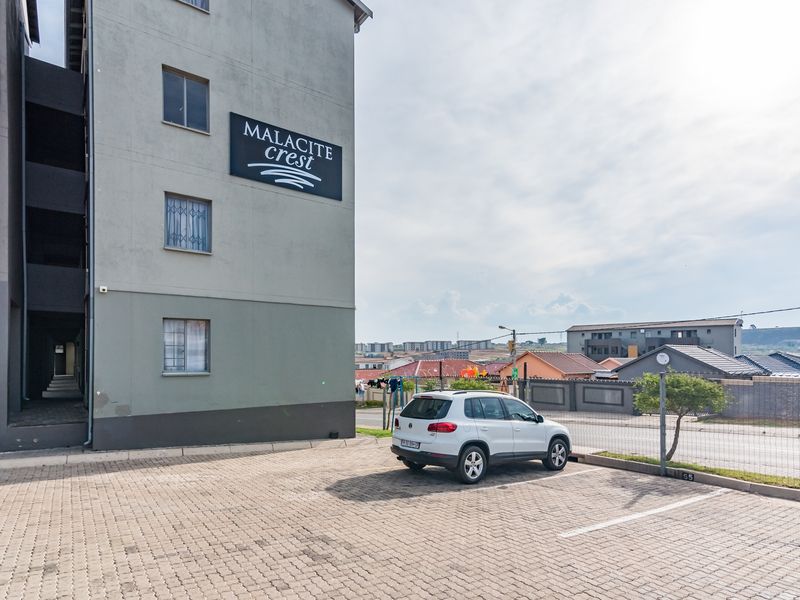 Exterior view of the Malacite Crest apartment complex featuring a paved parking area and secure perimeter fencing.