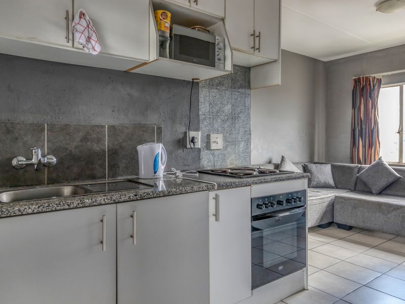 Open-plan kitchen and living area featuring granite countertops, built-in cabinetry, integrated oven and hob, and tiled flooring throughout.