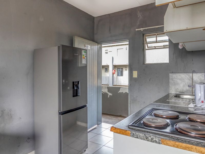 A compact kitchen featuring an electric hob, stainless steel sink, and tiled flooring, currently requiring cosmetic updates to the wall finishes and cabinetry.