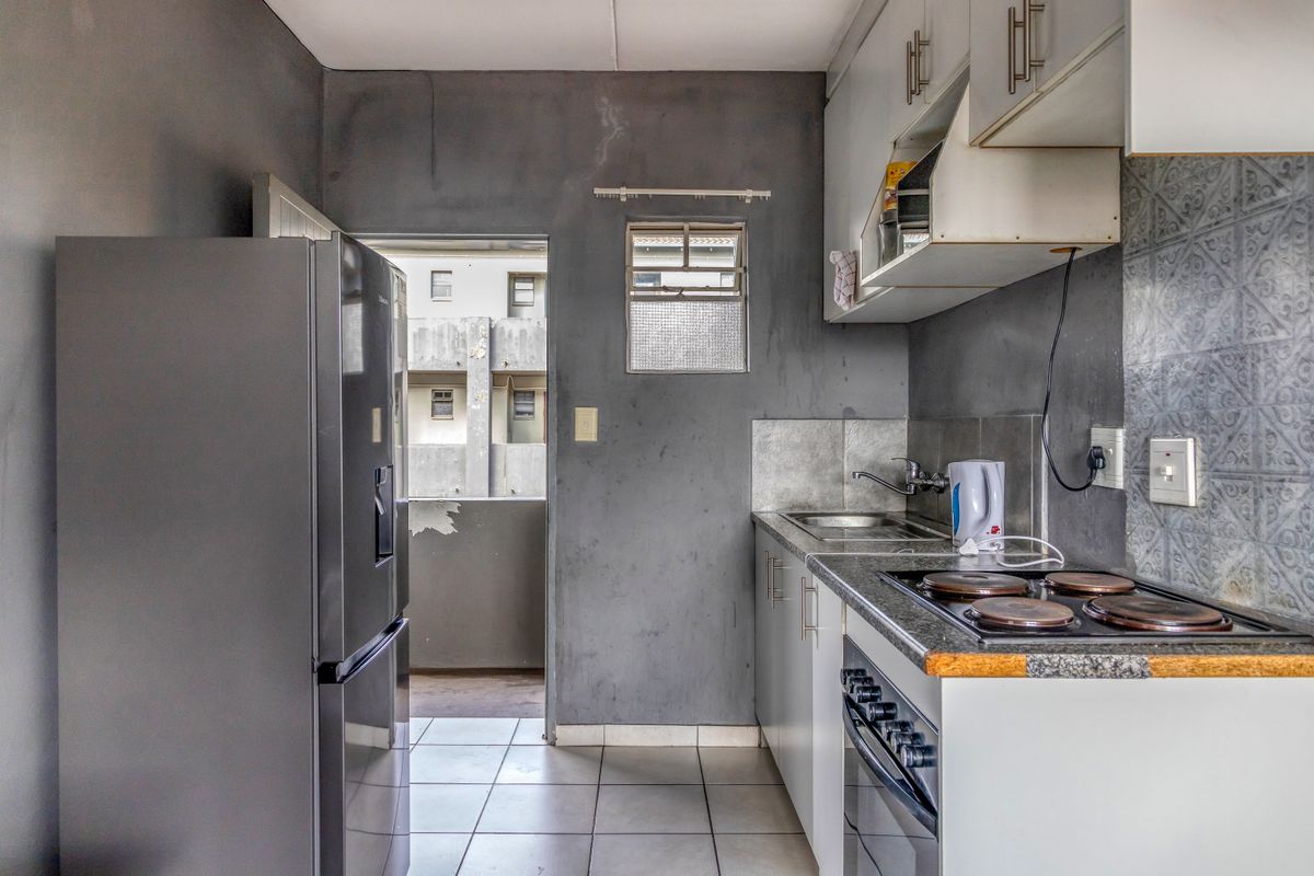 Compact kitchen featuring built-in cabinetry, an electric hob, oven, and tiled flooring, with direct access to an exterior balcony area.