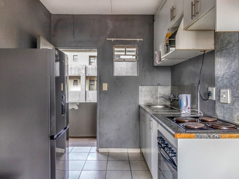 Compact kitchen featuring built-in cabinetry, an electric hob, oven, and tiled flooring, with direct access to an exterior balcony area.
