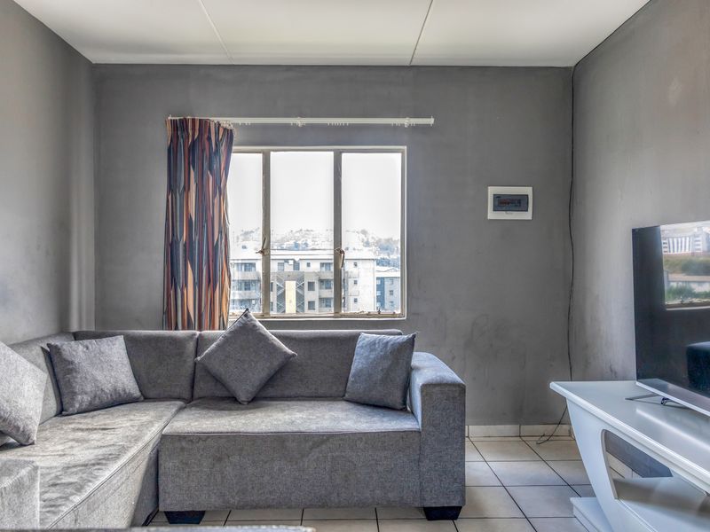 A living room featuring tiled flooring and a wall-mounted electrical distribution board, with neutral grey walls and natural light from the window.