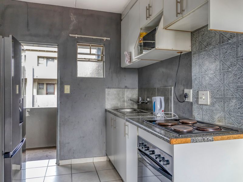 Compact kitchen featuring built-in cabinetry, granite countertops, an electric hob, and oven, with a tiled backsplash and direct access to an exterior balcony.
