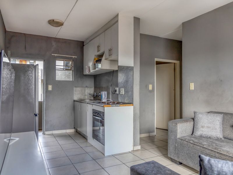 Open-plan living area featuring a compact kitchen with built-in cabinetry, oven, and hob, finished with tiled flooring throughout.