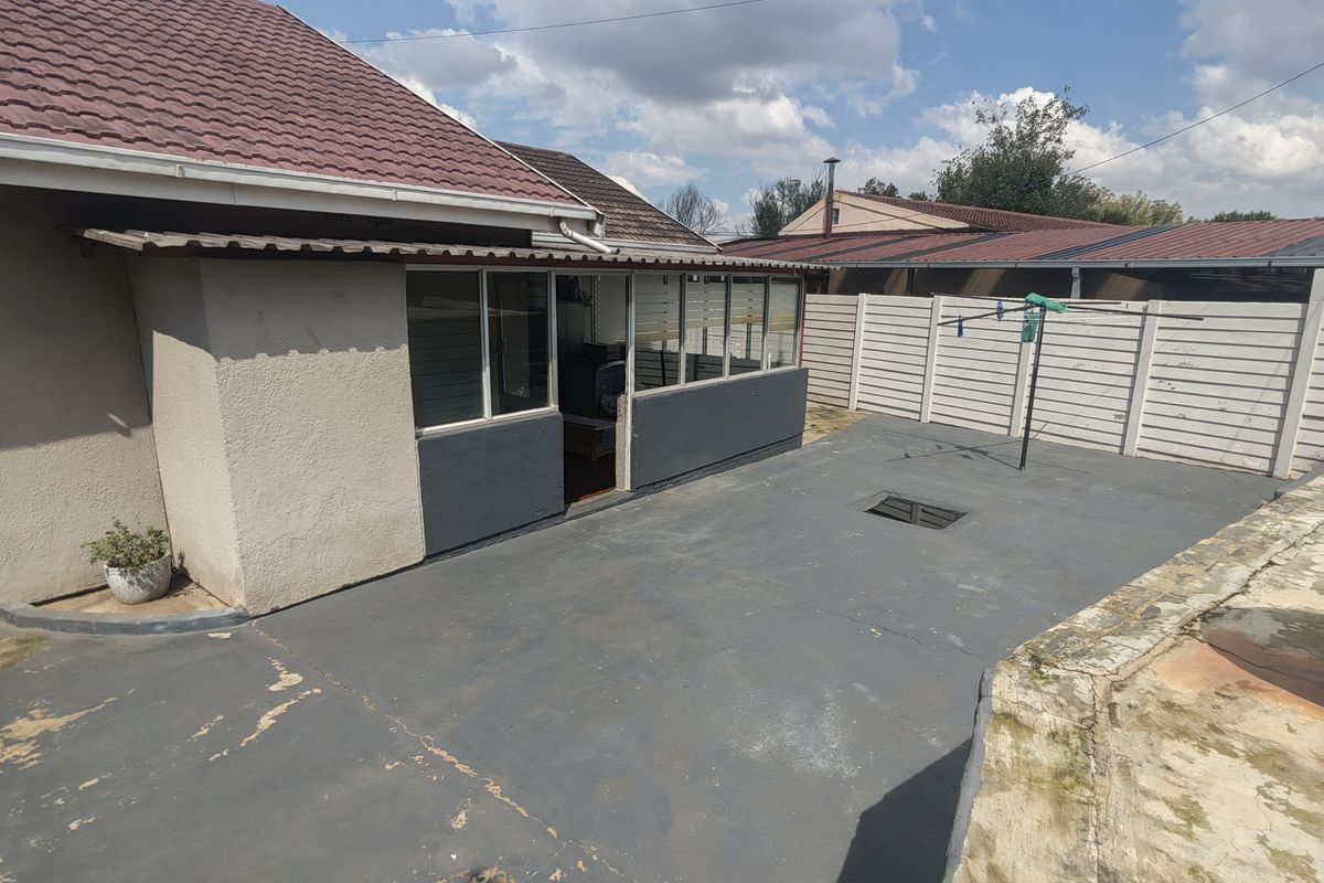 Rear exterior view featuring a paved patio area, enclosed patio structure, and precast concrete boundary walling under a tiled roof.