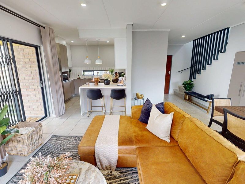 Modern open-plan living area featuring a sleek kitchen with island, tiled floors, and a staircase with a contemporary metal balustrade.