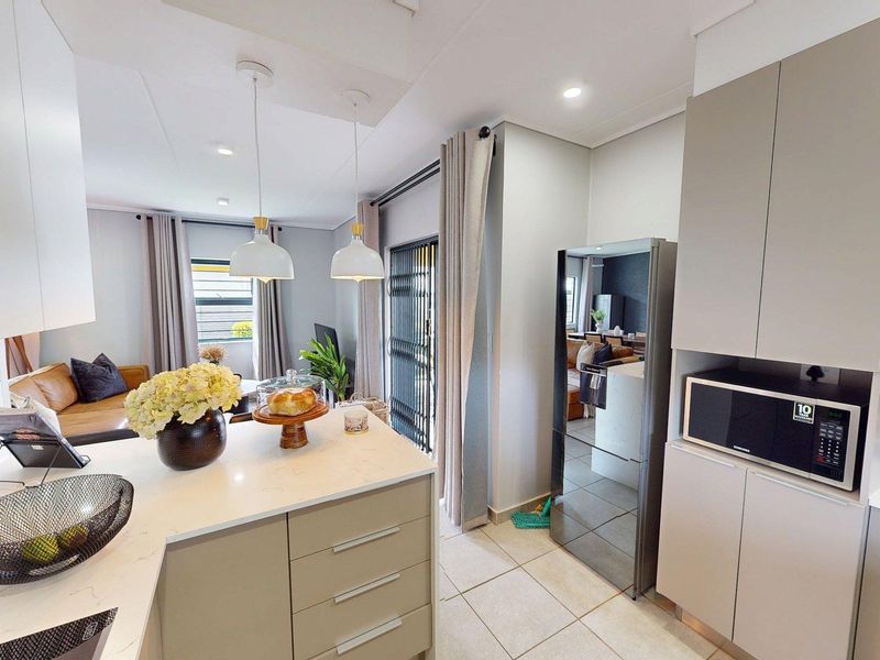 Modern open-plan kitchen featuring sleek cabinetry, quartz countertops, built-in microwave, and tiled flooring, seamlessly flowing into the adjacent living area.