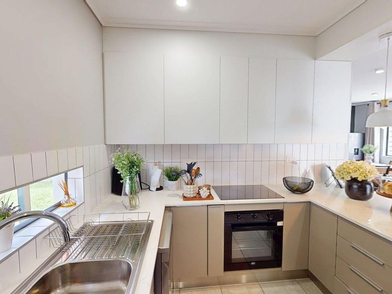 Modern kitchen featuring sleek cabinetry, stone countertops, integrated electric hob, built-in oven, and a tiled splashback with a convenient window view.